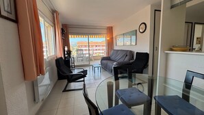 A modern living room with a sofa, chairs, a glass table, and a balcony with a view. - Apartment 'Blaumar B310' with Shared Pool, Private Terrace and Wi-Fi (LÈstartit)