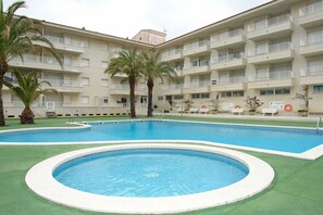 A hotel with a large outdoor swimming pool, multiple balconies, and palm trees.