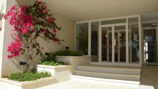 A building entrance with a glass door, a concrete planter with greenery, and a pink flowering plant. - Apartment 'Blaumar B310' with Shared Pool, Private Terrace and Wi-Fi (LÈstartit)