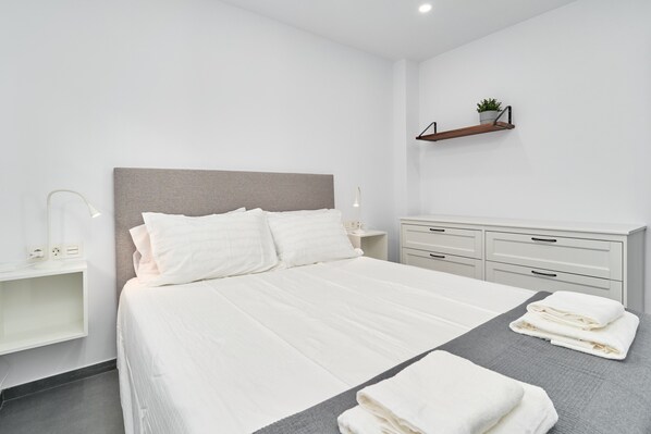 Un dormitorio moderno con cama, mesitas de noche, cómoda y estante con una planta.