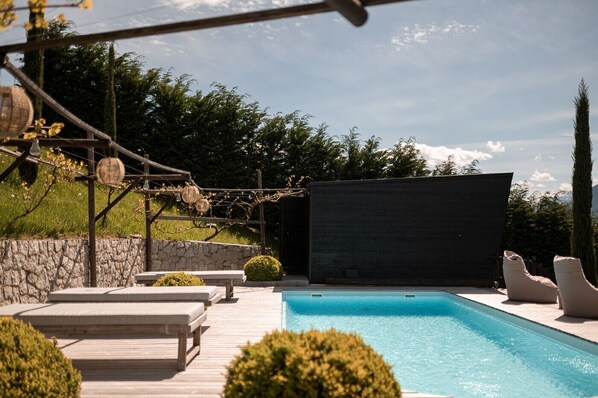 A swimming pool with lounge chairs, a stone wall, and a pergola with vines. - Chalet "Goyen" with Shared Pool, Private Terrace & Wi-Fi (Schenna)