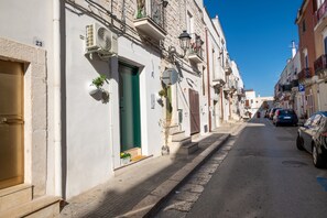 Une rue étroite bordée de bâtiments traditionnels, une voiture garée et un ciel bleu dégagé.