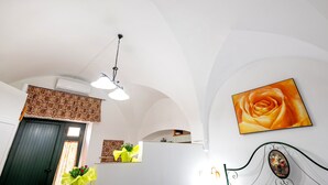 Een interieur met een donkere deur, een plafondlamp, een aan de muur hangend schilderij van een roos en een bed met een decoratief hoofdeinde.