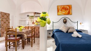 Een kamer met een bed, een eettafel met stoelen, een keukenhoek en een muur met een lijst erin.