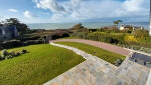 Un paisaje costero con un camino pavimentado, zonas verdes y vista al mar.