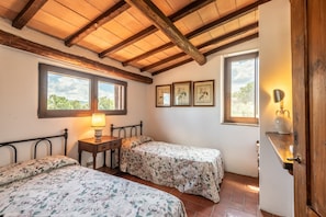 Ein Schlafzimmer mit zwei Betten, Holzbalken, Fenstern, einem Nachttisch mit Lampe und gerahmten Bildern an der Wand.