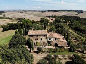Una casa de piedra con tejado de baldosas, rodeada de árboles y colinas ondulantes.