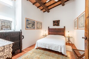 Un dormitorio con cama de madera, una mesita de noche con lámpara, cómoda y ventana con vistas.