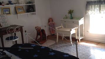 A bedroom with a bed, a desk, a chair, a rocking chair, a ceiling fan, and a window with curtains.
