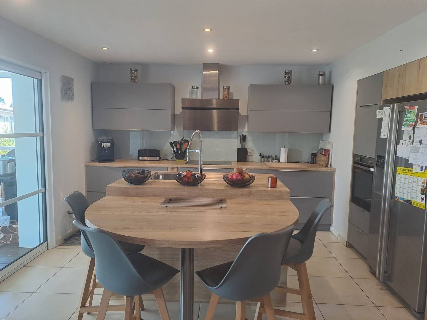 Una cocina moderna con una isla central, dos sillas azules y un refrigerador de acero inoxidable.