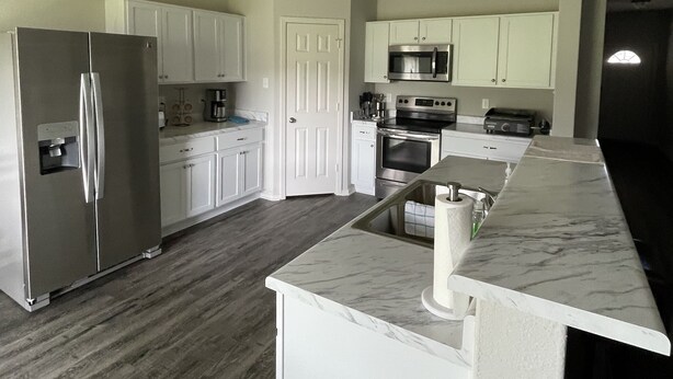 A modern kitchen with white cabinets, stainless steel appliances, and a marble countertop. - Like New Home close to town family friendly, quiet and close to amenities.  (Conway)