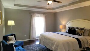 A bedroom with a bed, a ceiling fan, a window with curtains, and a blue armchair.