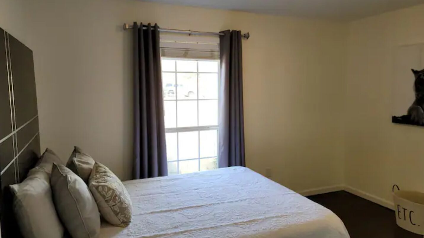 A bedroom with a bed, curtains, a window, and a wall-mounted shelf.