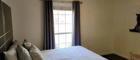 A bedroom with a bed, curtains, a window, and a wall-mounted shelf.