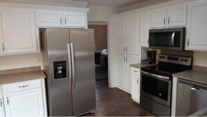 A kitchen with white cabinets, a stainless steel refrigerator, a microwave, an oven, and a dishwasher.