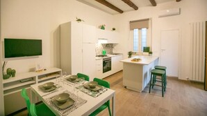 Una cuina compacta amb armaris blancs, una illa central i cadires verdes.