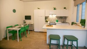 Una cuina moderna amb armaris blancs, una illa central i tamborets de bar verds.