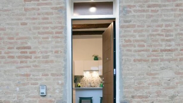 Accés estret a un edifici amb façana de maó, un petit escaló que mena a la porta, i dues plantes en testos a cada banda.