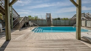 Una terraza de madera con piscina, una escalera y vista al océano.