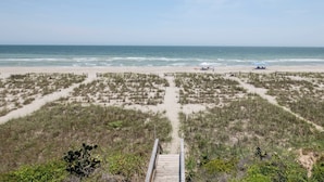 A beach with a wooden boardwalk leading to the shore, sandy dunes, and a clear view of the ocean. - Hobbs Realty - Enjoy "Southern Comfort" at it's best in this gorgeous oceanfront home! (Holden Beach)