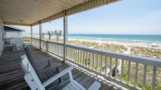 A covered deck with wooden railings overlooking a beach. - Hobbs Realty - Enjoy "Southern Comfort" at it's best in this gorgeous oceanfront home! (Holden Beach)