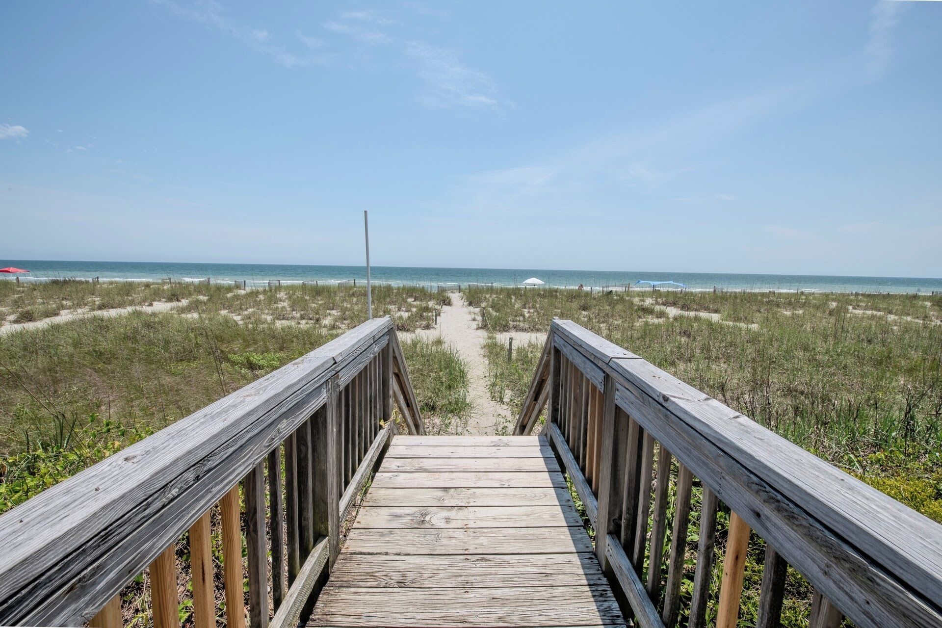 A wooden boardwalk leading to a beach with a clear view of the ocean.