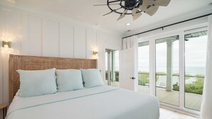 A bedroom with a large bed, a ceiling fan, and a view of the ocean through large sliding doors. - Hobbs Realty - Luxury Oceanfront Home w/Heated Pool, Elevator, and Media Room (Holden Beach)