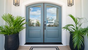 A double door with glass panels, flanked by two large potted plants, and a light-colored rug on the floor. - Hobbs Realty - Luxury Oceanfront Home w/Heated Pool, Elevator, and Media Room (Holden Beach)