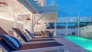 A poolside area with lounge chairs, a covered seating area, and a pool with a tiled deck.