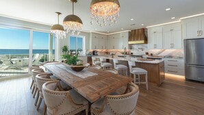 A modern kitchen with a large island, wooden dining table, and chairs, overlooking a scenic ocean view.