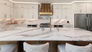 A modern kitchen with white cabinetry, a large marble island, stainless steel appliances, and a central island with bar stools.