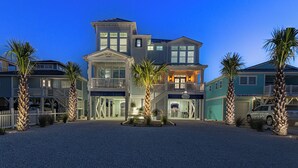 A large, multi-story beachfront property with a covered patio, a pool, and a beach house.