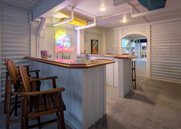 A bar area with wooden chairs, a neon sign, and a framed picture on the wall.