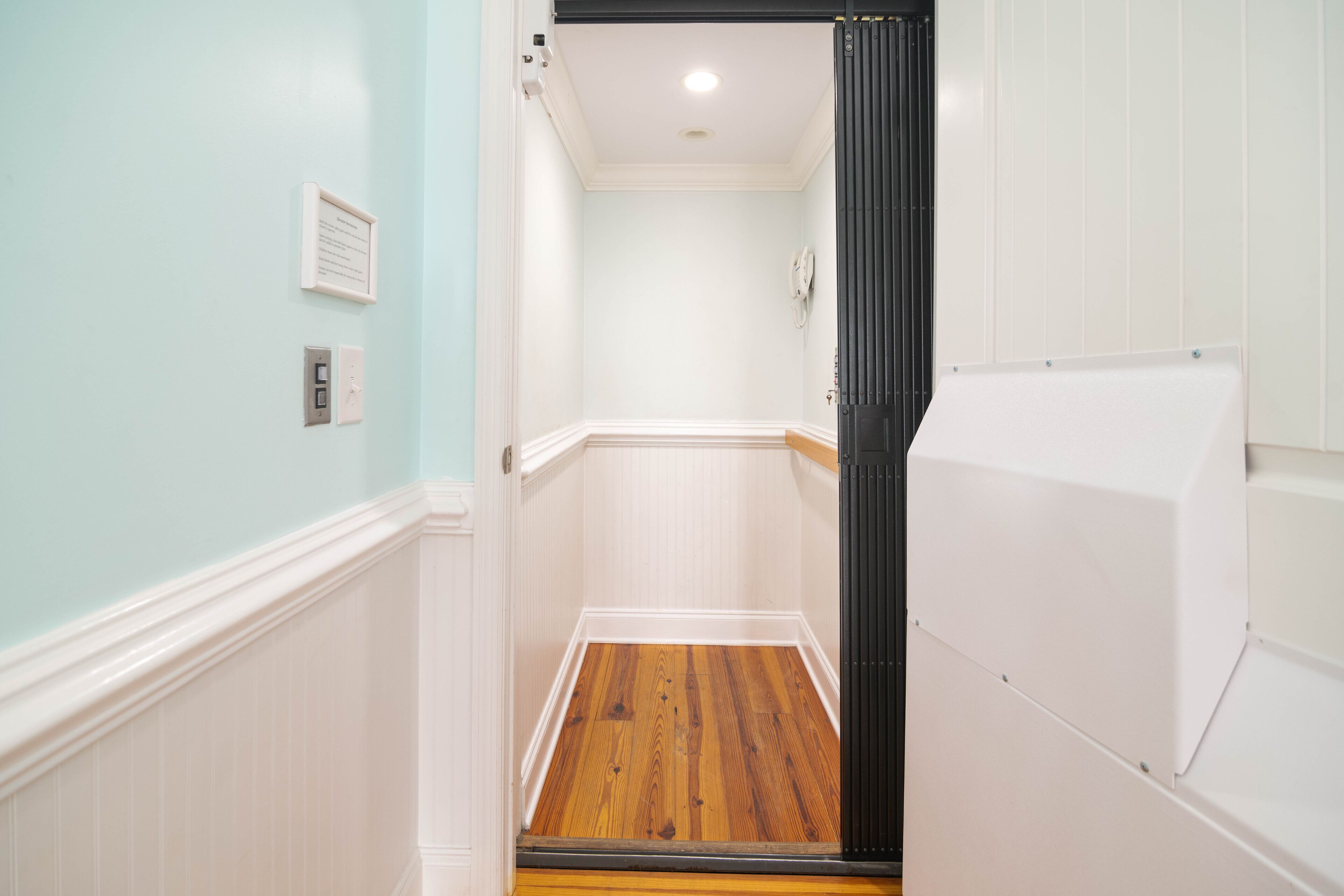 A narrow hallway with a wooden floor, white walls, and a black door.