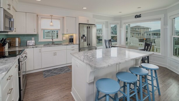 Una cocina moderna con armarios blancos, una isla grande con taburetes, un refrigerador y un comedor con vistas.