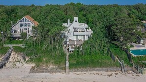 A large, modern house with multiple levels and a prominent chimney, surrounded by dense forest and a beach. - Water Front Property with Customized Pool and Spa with private access to the Delaware Bay (Villas)