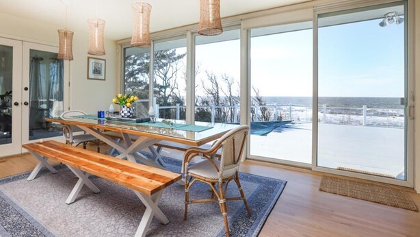 A dining area with a glass table, wooden bench, wicker chairs, and large windows overlooking a snowy landscape. - Water Front Property with Customized Pool and Spa with private access to the Delaware Bay (Villas)
