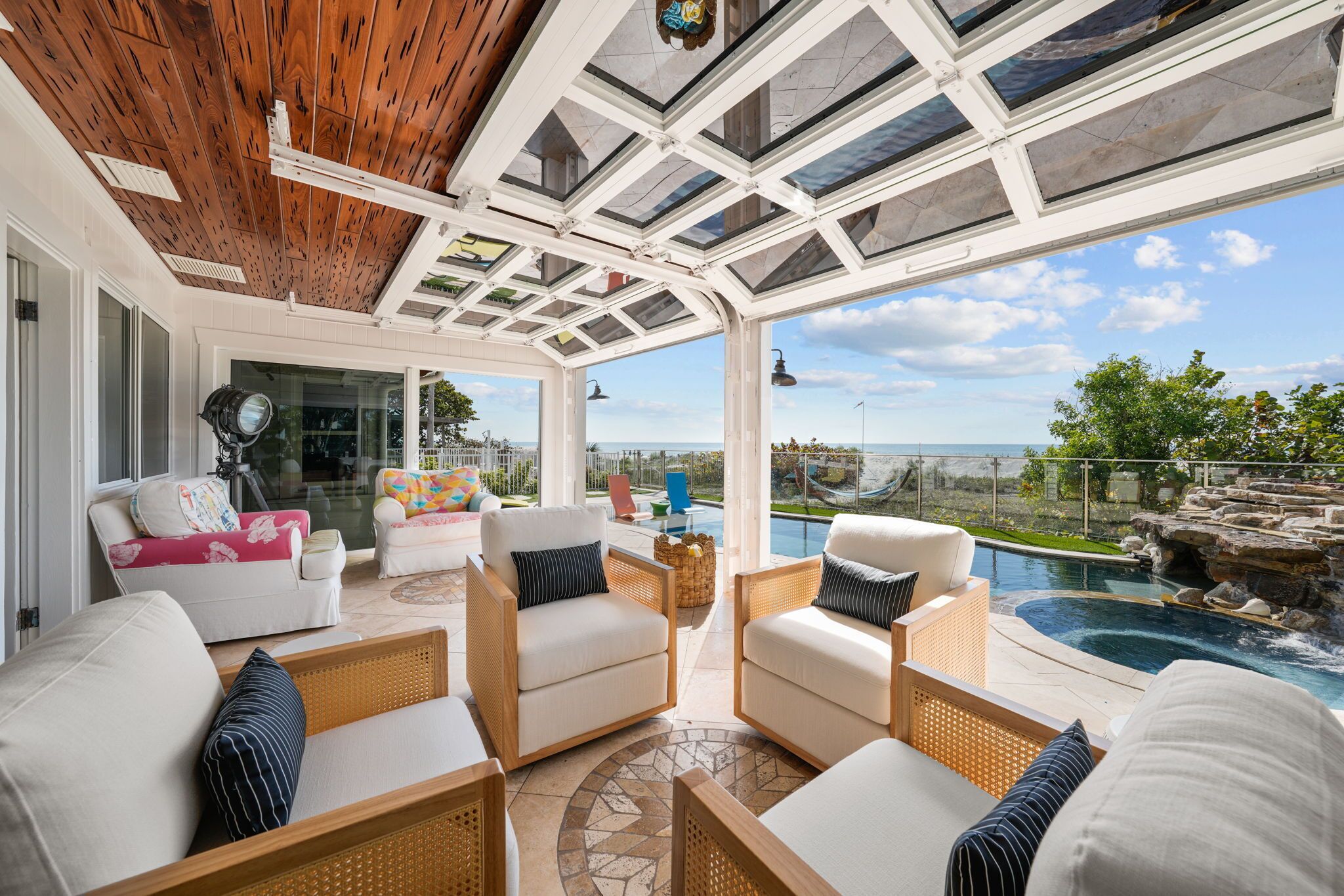 A sunlit patio with wicker furniture, a pool, and a view of the ocean.