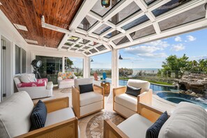Une terrasse ensoleillée, meublée de mobilier en osier, avec une piscine et une vue sur l’océan.