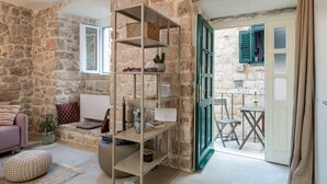 A cozy room with a stone wall, a wooden bookshelf, a comfortable sofa, and a small table with a chair. - MIRABILIS - studio apartment - Old Town (Dubrovnik)