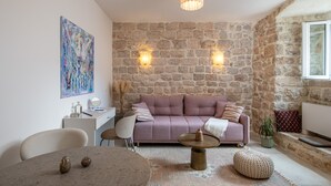 A cozy living room with a stone wall, a pink sofa, a round coffee table, and a pendant light. - MIRABILIS - studio apartment - Old Town (Dubrovnik)