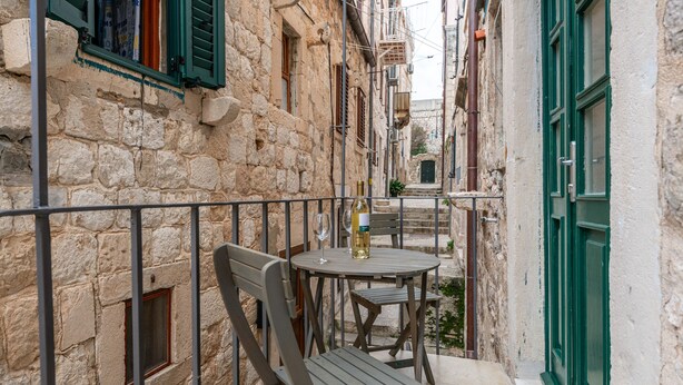 A balcony with a table and chairs, a bottle of wine, and a window with green shutters. - MIRABILIS - studio apartment - Old Town (Dubrovnik)