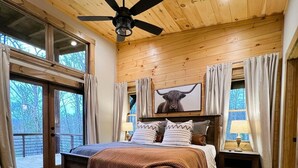 A bedroom with a bed, wooden ceiling, ceiling fan, large windows, and a view of the outdoors. - JULY DISCOUNT! New Modern Luxury Cabin- Hot Tub, Game Room, Fire Pit (Blue Ridge)