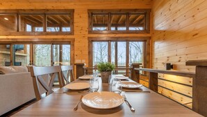 A wooden dining table set for four with a plant centerpiece, large windows, and a view of trees. - JULY DISCOUNT! New Modern Luxury Cabin- Hot Tub, Game Room, Fire Pit (Blue Ridge)