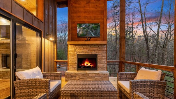 A cozy outdoor seating area with wicker furniture and a stone fireplace. - JULY DISCOUNT! New Modern Luxury Cabin- Hot Tub, Game Room, Fire Pit (Blue Ridge)