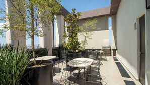 An outdoor patio with tables and chairs, surrounded by potted plants and a view of the city. - Tribu Coordenada Lafayette (Guadalajara)