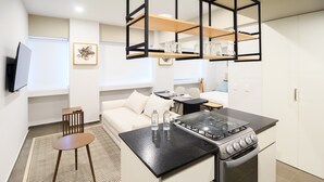 A modern kitchen with a gas stove, a dining area with a sofa, and a TV mounted on the wall. - Tribu Coordenada Lafayette (Guadalajara)