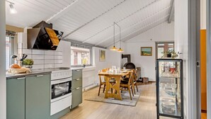 Eine Küche mit einer zentralen Kochinsel, einem Holztisch und Stühlen. Ein Glaskabinett enthält Geschirr.