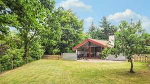 Ein modernes Haus mit Wintergarten, umgeben von einem gepflegten Rasen und reifen Bäumen.