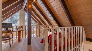 A cozy attic bedroom with a wooden ceiling, a desk with a chair, and a crib with a red blanket. - Spacious, newly remodeled, perfect location w/BBQ, Hot Tub, pool table, SmartTV (Carnelian Bay)